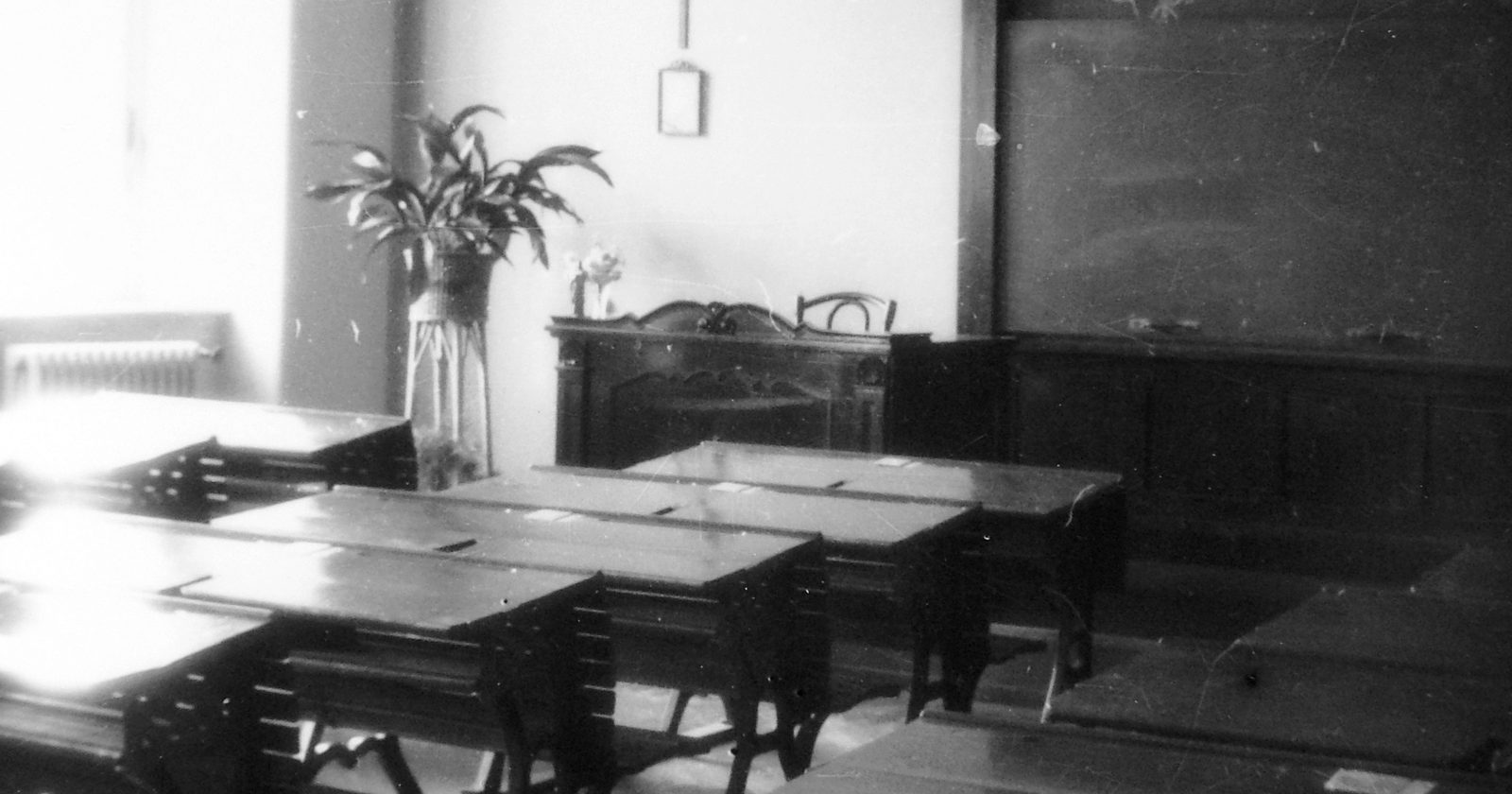 Pusta sala lekcyjna z rzędami drewnianych ławek, tablicą i krzyżem zawieszonym na ścianie